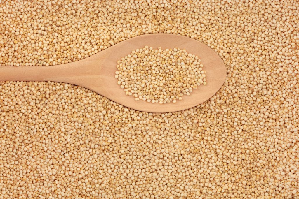 Quinoa cereal grains in a wooden spoon and forming a textured background. Very high in protein.